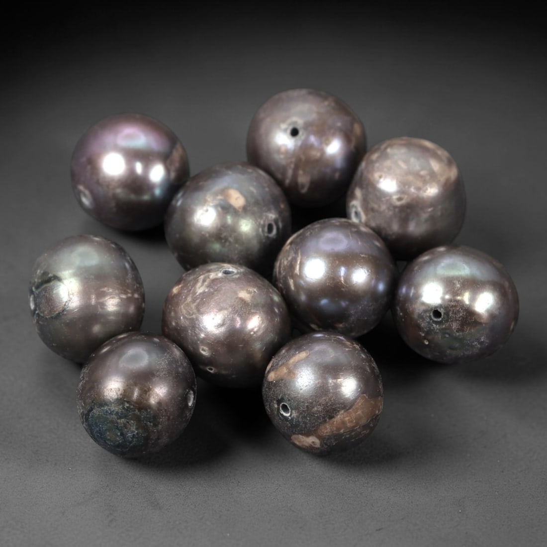 A Group of Ten Baroque Cultured Pearls, 94ZH: Comprising ten baroque cultured pearls, each of spherical to slightly irregular form with a deep metallic brown hue and subtle iridescent overtones. Each pearl features a small, precisely drilled hole