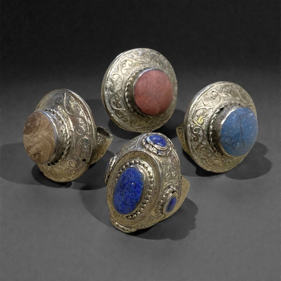 A Group of Four Antique Silvered Bronze Rings, 19th Century, Size 7-8US, 70g, 68AA: Each ring is crafted from silvered bronze, featuring ornate metalwork including filigree, repousse, and granulation details. The bezels are set with composite stones, the surfaces exhibit minor patina