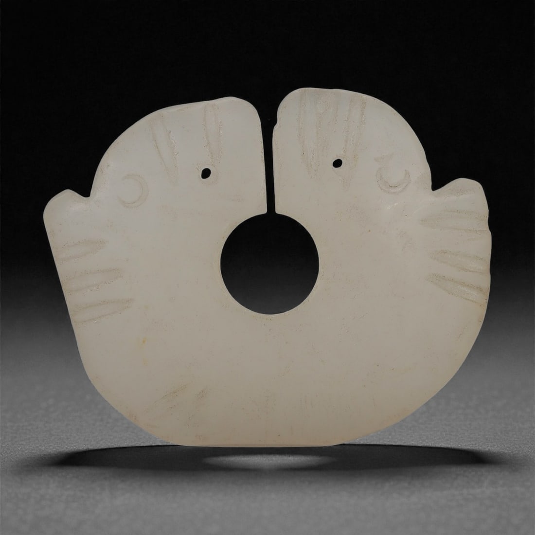 A Chinese Pale Jade Openwork Pendant with Confronted Birds, 20th Century, 69FD: Carved from pale off-white jade of even tone with soft translucency, the pendant is worked as a flattened symmetrical form depicting two confronted bird profiles arranged back-to-back around a central