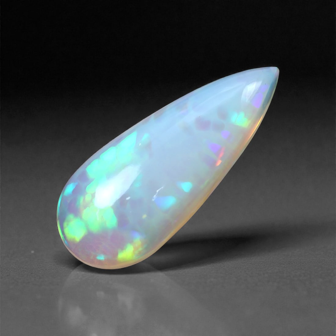 4.86 Carats Elongated Cabochon Opal - Natural Ethiopian Stone 21.8x9x5.7mm, 29XH: This sleek, elongated cabochon opal offers a mesmerizing play-of-color in a cascade of glowing greens, purples, and flickers of neon orange beneath a milky translucent body. The gem's teardrop form is