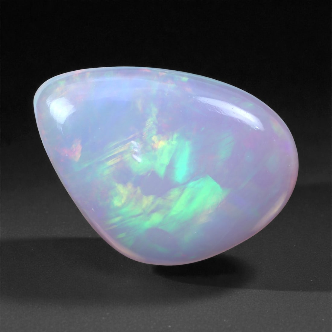 7.07 Carats Freeform Cabochon Opal - Natural Ethiopian Stone 14.9x13.8x5mm, 11XH: This beautifully contoured freeform Welo opal dazzles with radiant bursts of green fire, aqua, and subtle flashes of lavender and coral, all suspended within a translucent lavender body. The stone's a