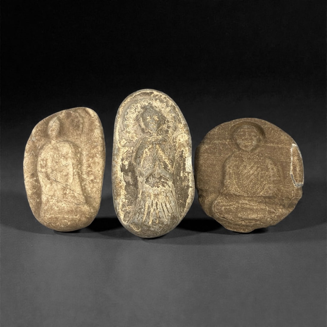 A Group of Three Edo Period Buddhist Stone Carvings, 17th-19th Century, 22FN: Carved from stone with natural tonal variation, surface wear, and mineral encrustation, the three objects depict Buddhist figures in shallow relief, set within irregular stone matrices. The leftmost c