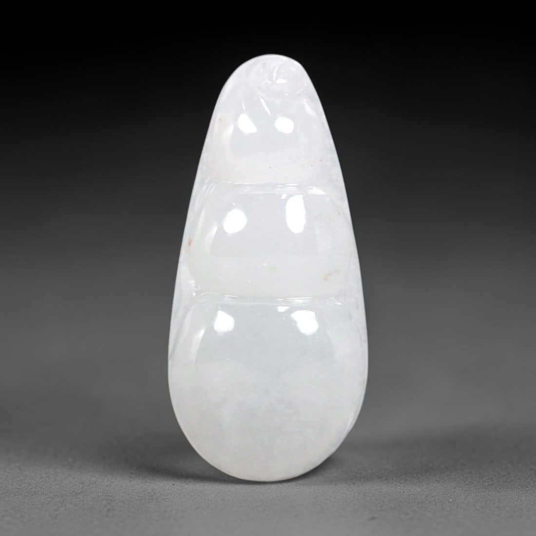 A Chinese Icy Jadeite Jade Bean Pendant, 20th Century, 60AB: Carved from translucent icy jadeite with a pale milky-white hue and minor natural inclusions, the pendant is shaped as a stylized three-segmented bean pod. Smooth, rounded contours define each segment
