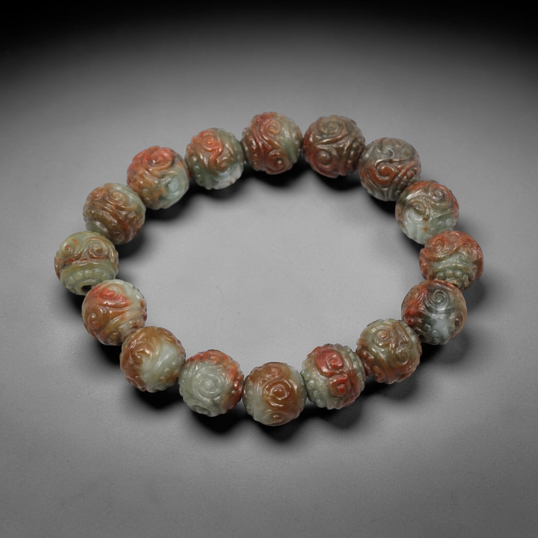 A Chinese Carved Jadeite Jade Bead Bracelet, 20th Century, 28ZK: Composed of a single strand of spherical jadeite jade beads, each elaborately carved with classic scrolling cloud and ruyi patterns, forming a circular bracelet. The beads exhibit striking natural pol