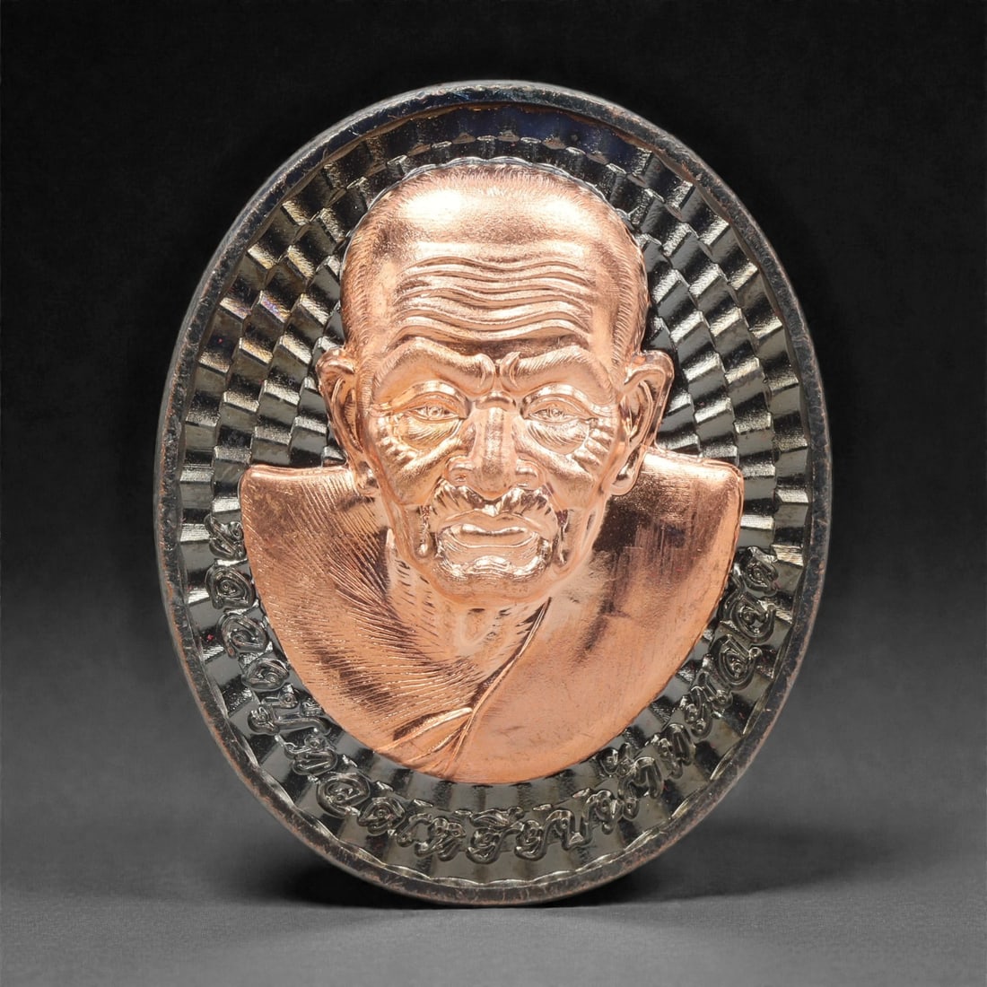 A Thai Bi-Metallic Monk Portrait Medallion, 21st Century, 90FP: Cast with a bi-metallic construction, the medallion is oval and double-sided with a raised silver-toned metal border. The obverse features a high-relief bust portrait of a Buddhist monk rendered in co
