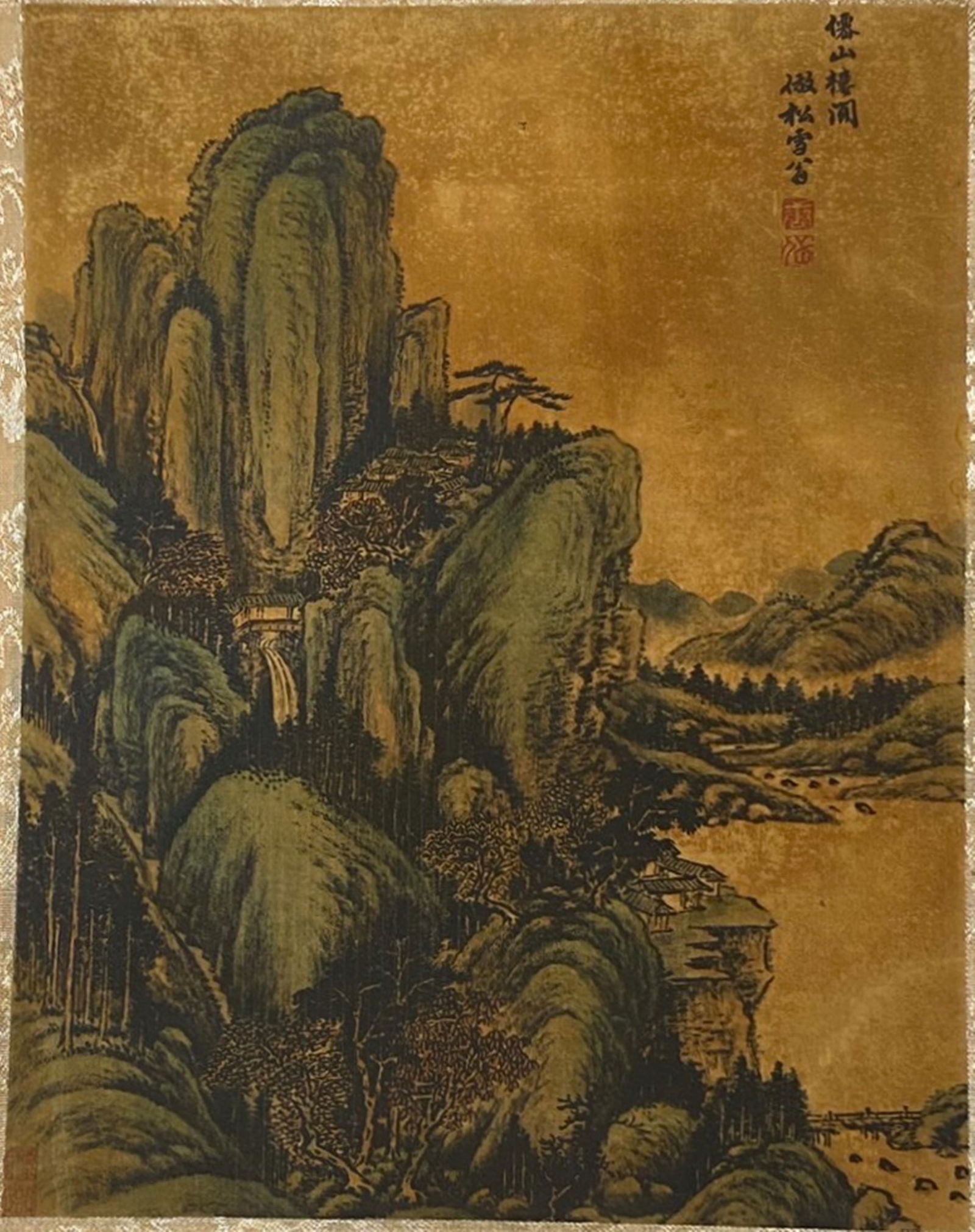 A Chinese Ink and Color Textile Print, Pavilions Among Green Peaks, 20th Century, 41FK: Printed on woven silk or hemp textile with a gold-toned ground, the composition depicts a towering mountain landscape in the Northern Song style. Steep, verdant cliffs dominate the scene, with a hidde