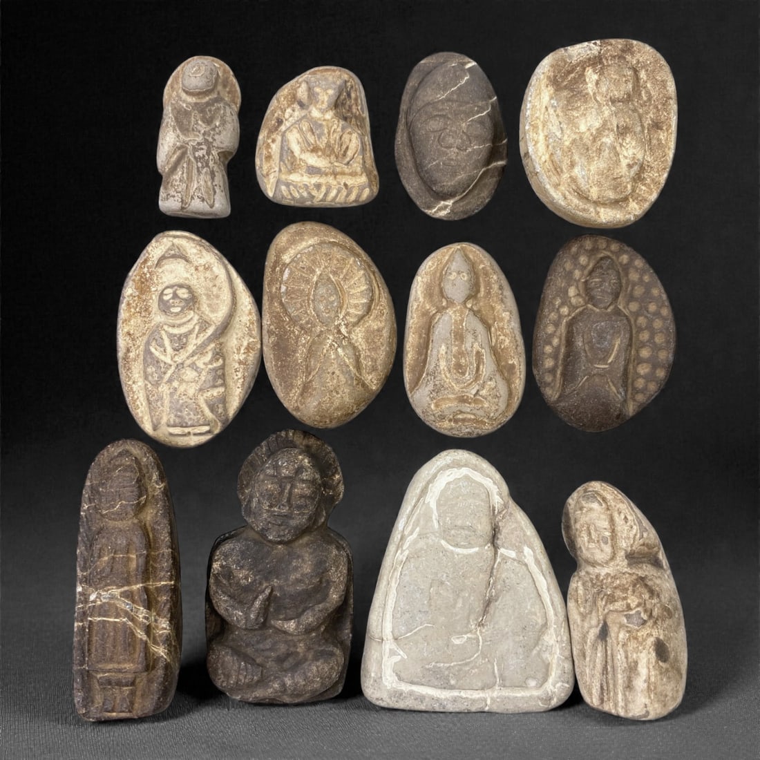 A Japanese Stone Buddhist Figure Group, Edo Period, 76XJ: Comprising twelve small stone figures carved from light to dark-toned stone with natural inclusions and surface wear, the group includes seated and standing Buddhist figures rendered in low to moderat