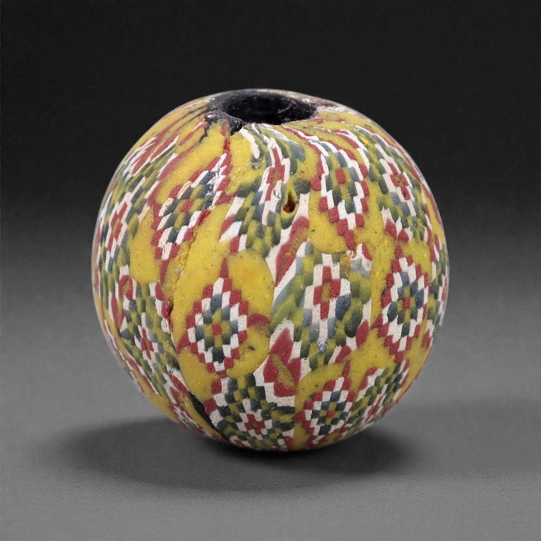 Ancient Glass Bead - Roman Mosaic Cane Sphere, 26Z: This spherical glass bead is formed from a yellow ground densely inlaid with elongated mosaic cane segments, fused and drawn into a continuous patterned surface using Roman glassworking techniques. Th