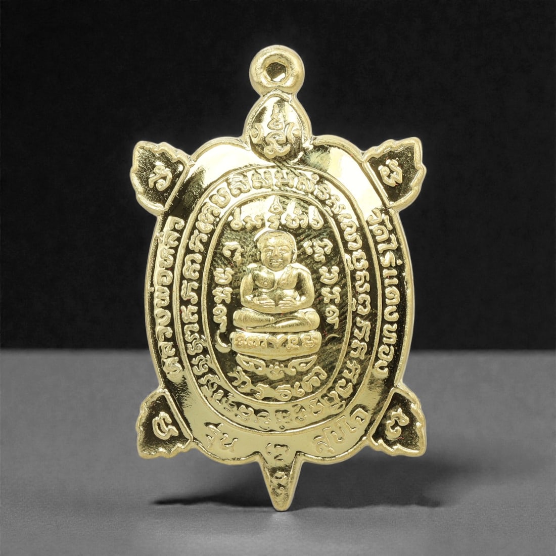 A Thai Gilt-Metal Turtle-Form Amulet, 21st Century, 72FP: Cast from metal with a gilt surface finish, the amulet is shaped as a turtle with an integral suspension loop at the apex. The obverse features a central seated Buddha figure in cross-legged meditatio