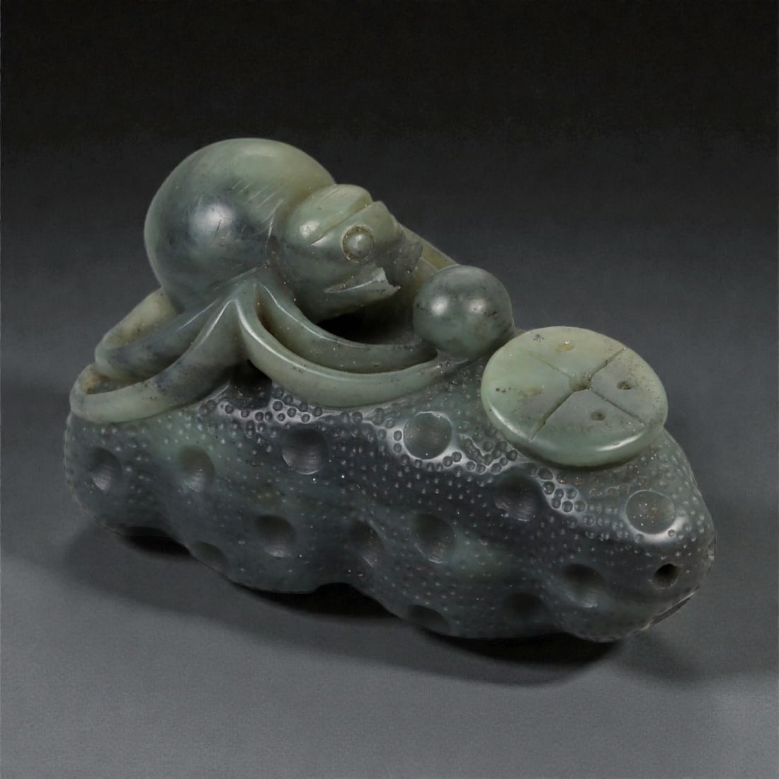 A Chinese Nephrite Jade Spider Carving, 20th Century, 77FB: Carved from dark green nephrite jade with mottled inclusions and areas of lighter translucency, the object is modeled as a spider resting upon a textured ground. The spider is carved in the round, wit