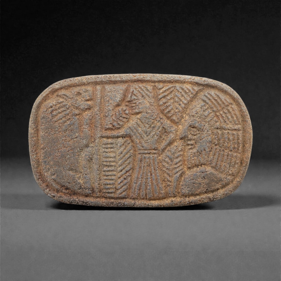 Ancient Near Eastern Lapis Lazuli Relief Plaque, 2nd-1st Millennium BCE, 81FM: An oval lapis lazuli relief plaque, measuring 8.5 x 5 cm, with a deep blue matrix and visible calcite inclusions, exhibiting natural surface patina and wear. The plaque depicts a narrative scene in sh