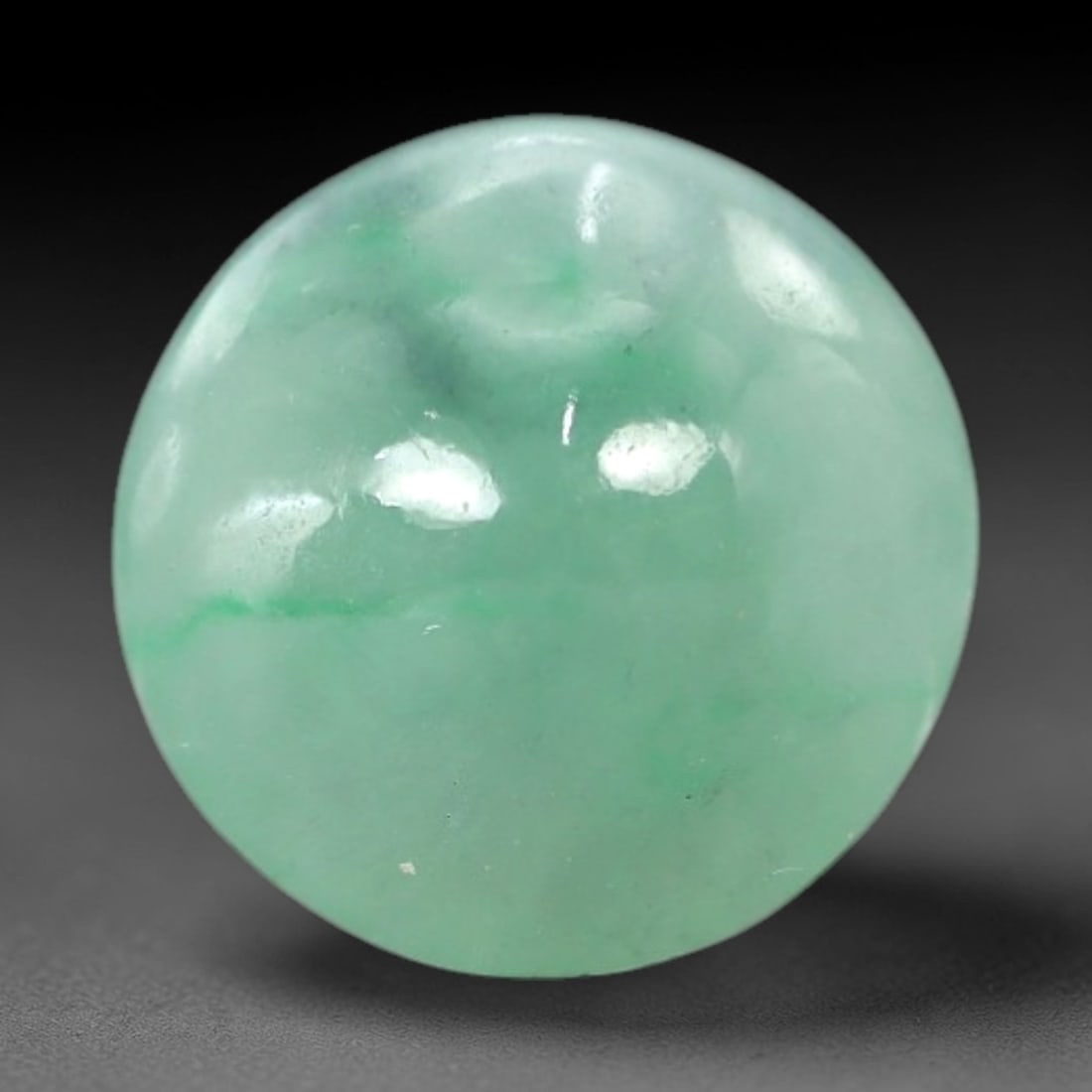 5.54 Carats Apple Green Jadeite Cabochon - Natural Burmese Stone, 91AB: This near-round jadeite cabochon features a variegated apple green hue, with subtle verdant inclusions and a distinct green line distributed throughout a pale, semi-translucent matrix. The domed caboc