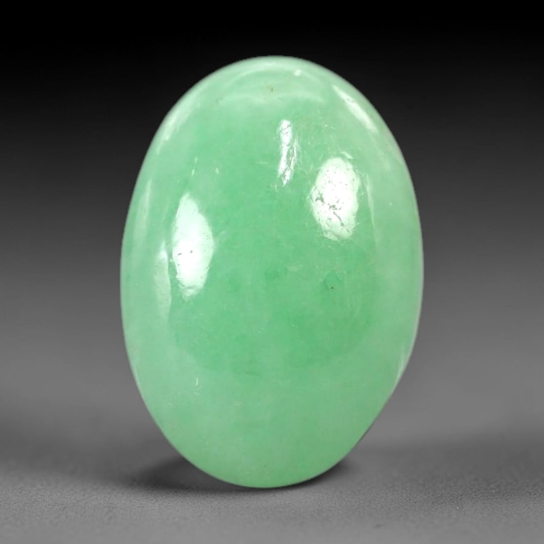3.93 Carats Apple Green Jadeite Cabochon - Natural Burmese Stone, 92AB: This elongated oval jadeite cabochon features a consistent, vivid apple green hue with a polished surface that yields a distinct waxy luster. The domed cabochon cut is calibrated to the stone's natura