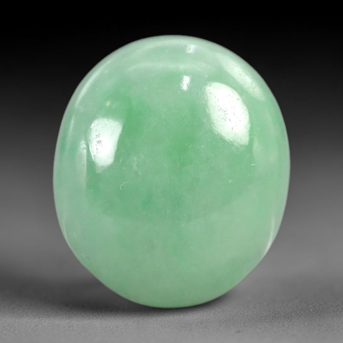 7.32 Carats Apple Green Jadeite Cabochon - Natural Burmese Stone, 3AC: This oval jadeite cabochon exhibits a rich, even apple green hue with a smooth, polished surface that reflects light with a soft, luminous quality. The domed cabochon cut enhances the stone's transluc