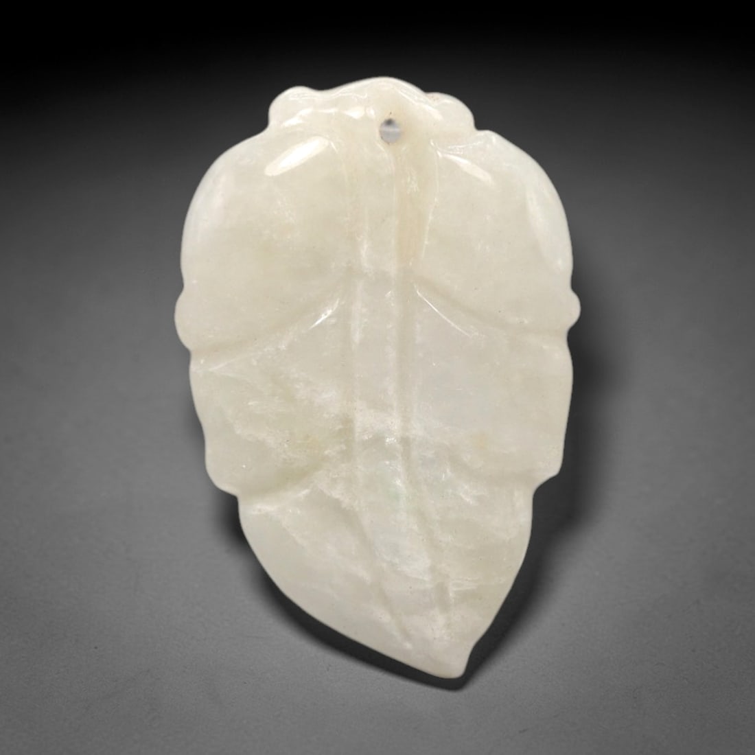 A Chinese Jadeite Jade Leaf-Form Pendant, 20th Century, 78FR: Carved from opaque white jadeite jade with subtle natural granular inclusions, the pendant is shaped in the form of a stylized leaf. A central vertical raised ridge divides the two lobes, with shallow