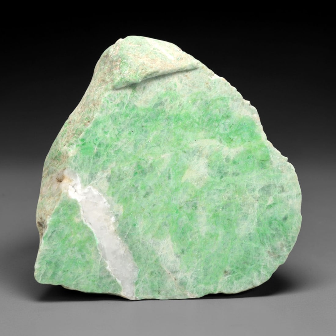 A Burmese Jadeite Jade Rough, 20th Century, 58FS: A piece of Burmese jadeite jade rough, with a pale greenish-white matrix and vibrant green mineral inclusions. The rough is shaped as an irregular, angular form, with visible natural fractures and a p