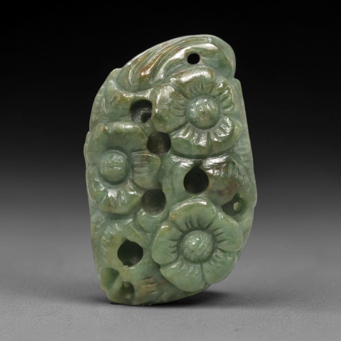 A Chinese Jadeite Jade Floral Pendant Plaque, 20th Century, 15FR: Carved from uniform celadon jadeite jade with subtle brownish inclusions and a glossy finish, the pendant is formed as an irregularly shaped, flattened plaque. The surface is executed in high relief a