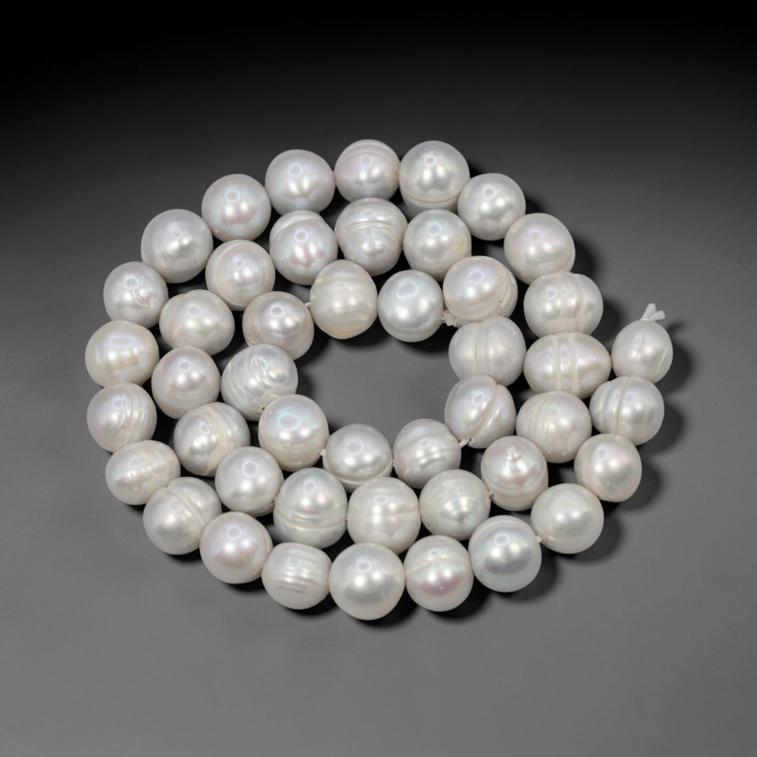 A Strand of Cultured Pearls, 20th Century, 85ZJ: Composed of near-round cultured pearls with a silvery-white body color and distinct iridescent overtones, the strand is strung in a single continuous line. Each pearl exhibits a smooth, high-luster su