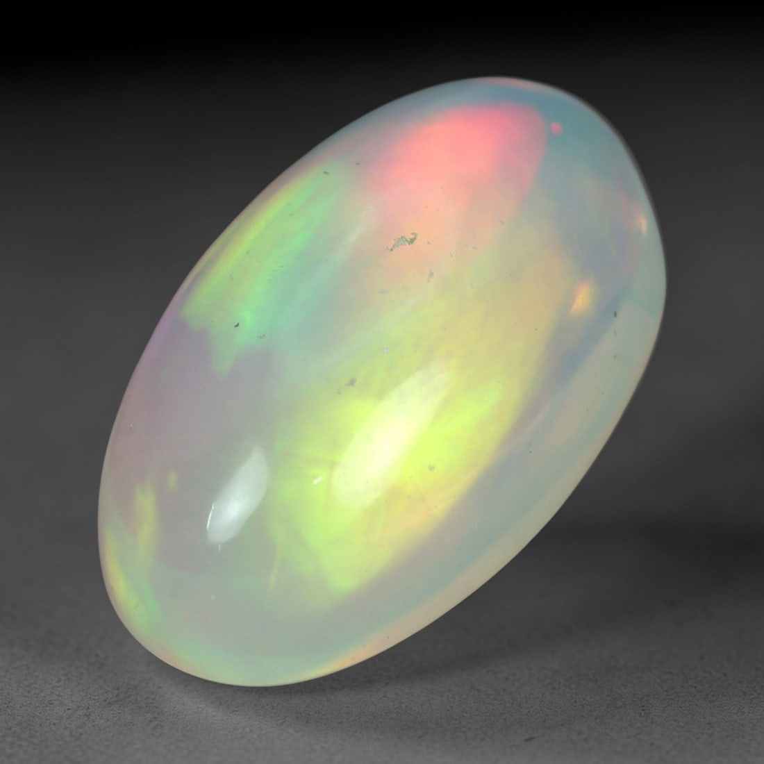 5.22 Carats Multicolor Iridescent Welo Opal Cabochon - Natural Ethiopian 16x9mm, 75XM: This luminous Welo opal cabochon radiates with a soft, milky translucence, its pale, creamy base alive with a vivid play of color. Bold flashes of peachy-pink, vibrant green, and golden yellow shift a