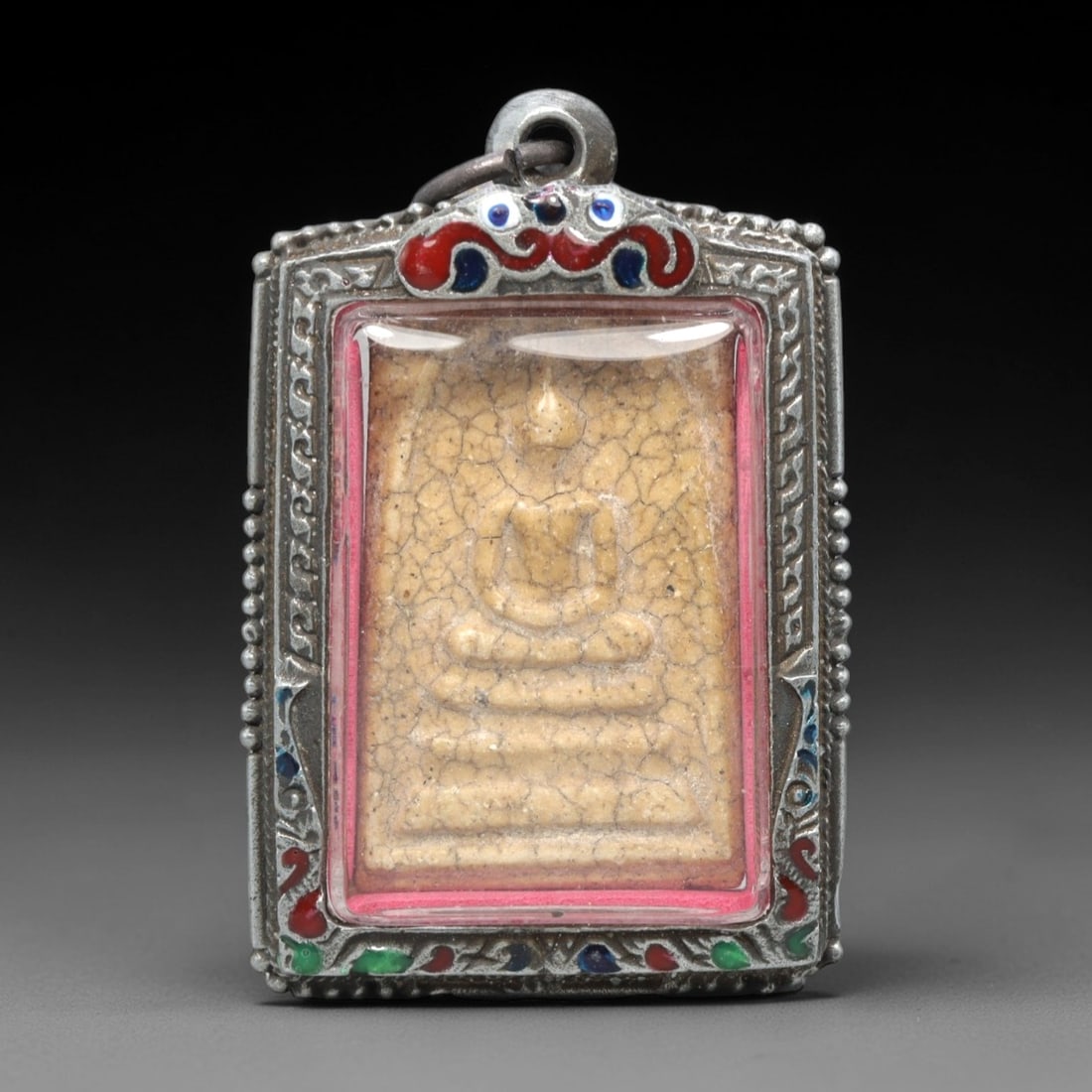 A Thai Phra Somdet Clay Amulet in an Enameled Silver-Tone Case, 20th Century, 12ZK: This rectangular Phra Somdet amulet is crafted from sacred beige clay and encased in an ornate silver-tone metal case with a suspension loop at the apex. The obverse of the case is adorned with vibran