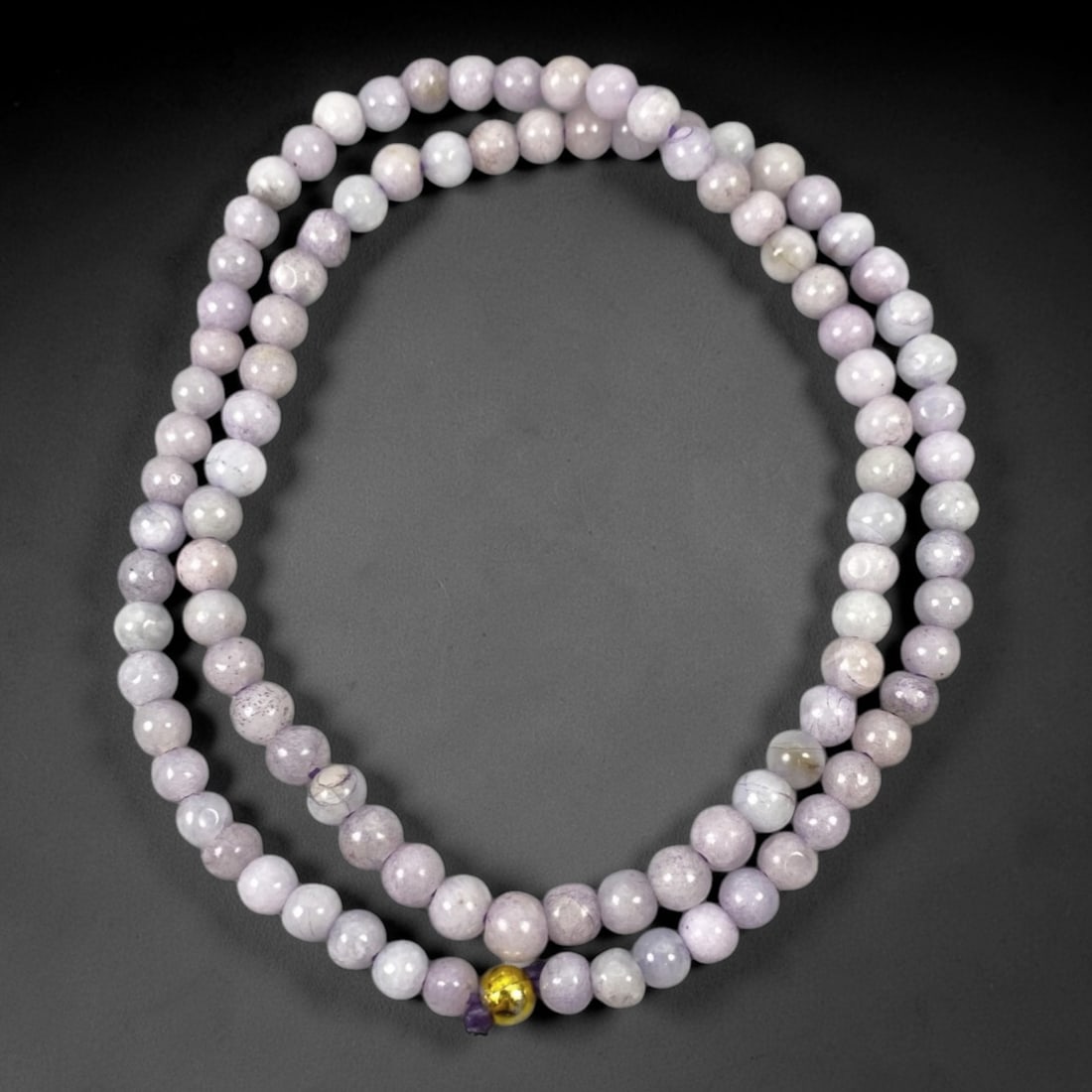 A Chinese Jadeite Jade Bead Necklace, 20th Century, 68ZK: Composed of spherical beads of pale lavender and white jadeite jade with natural veining and subtle tonal variations, the necklace is strung in a continuous loop. The beads exhibit a smooth, polished