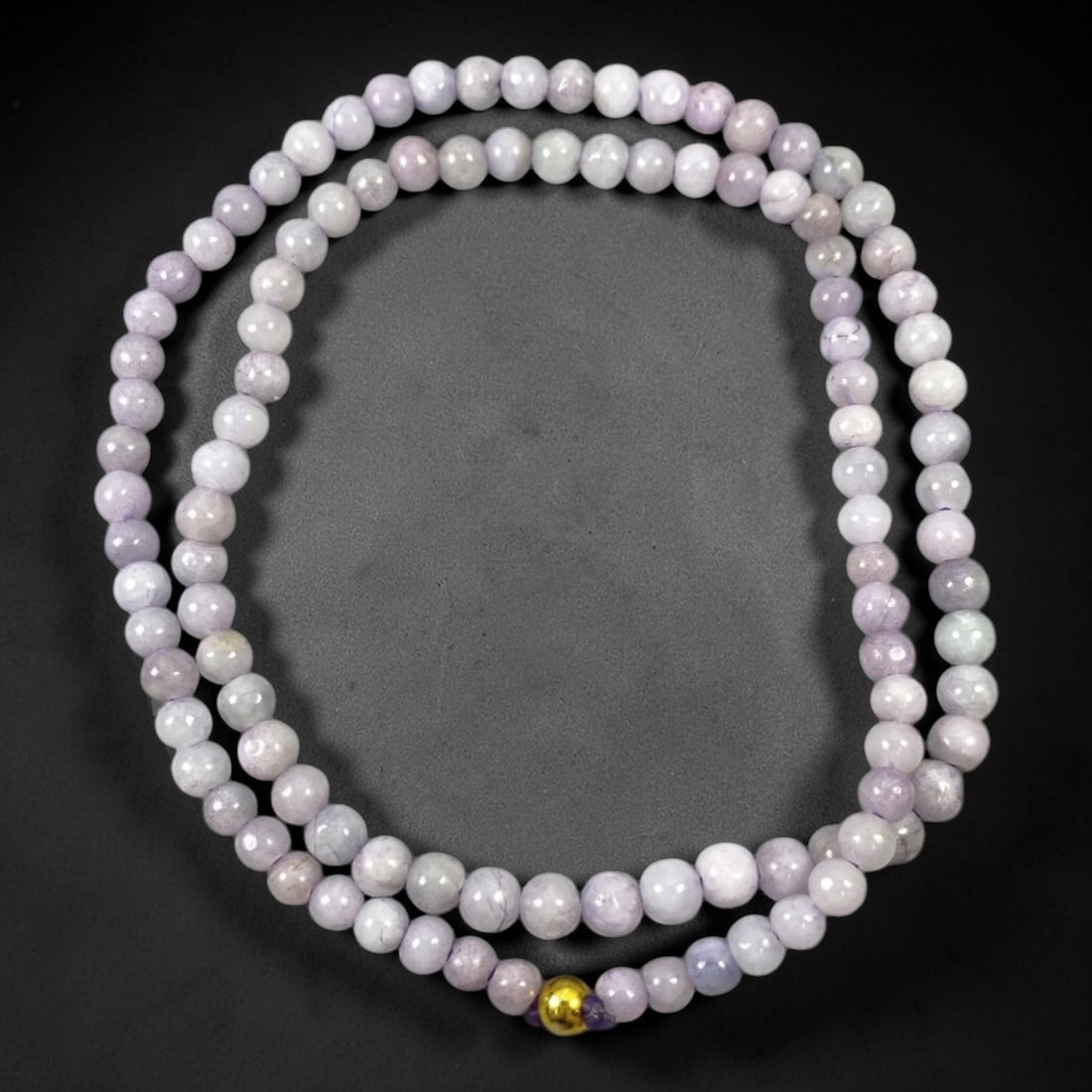 A Chinese Jadeite Jade Bead Necklace, 20th Century, 71ZK: Composed of spherical beads of pale lavender and white jadeite jade with natural veining and subtle tonal variations, the necklace is strung in a continuous loop. The beads exhibit a smooth, polished