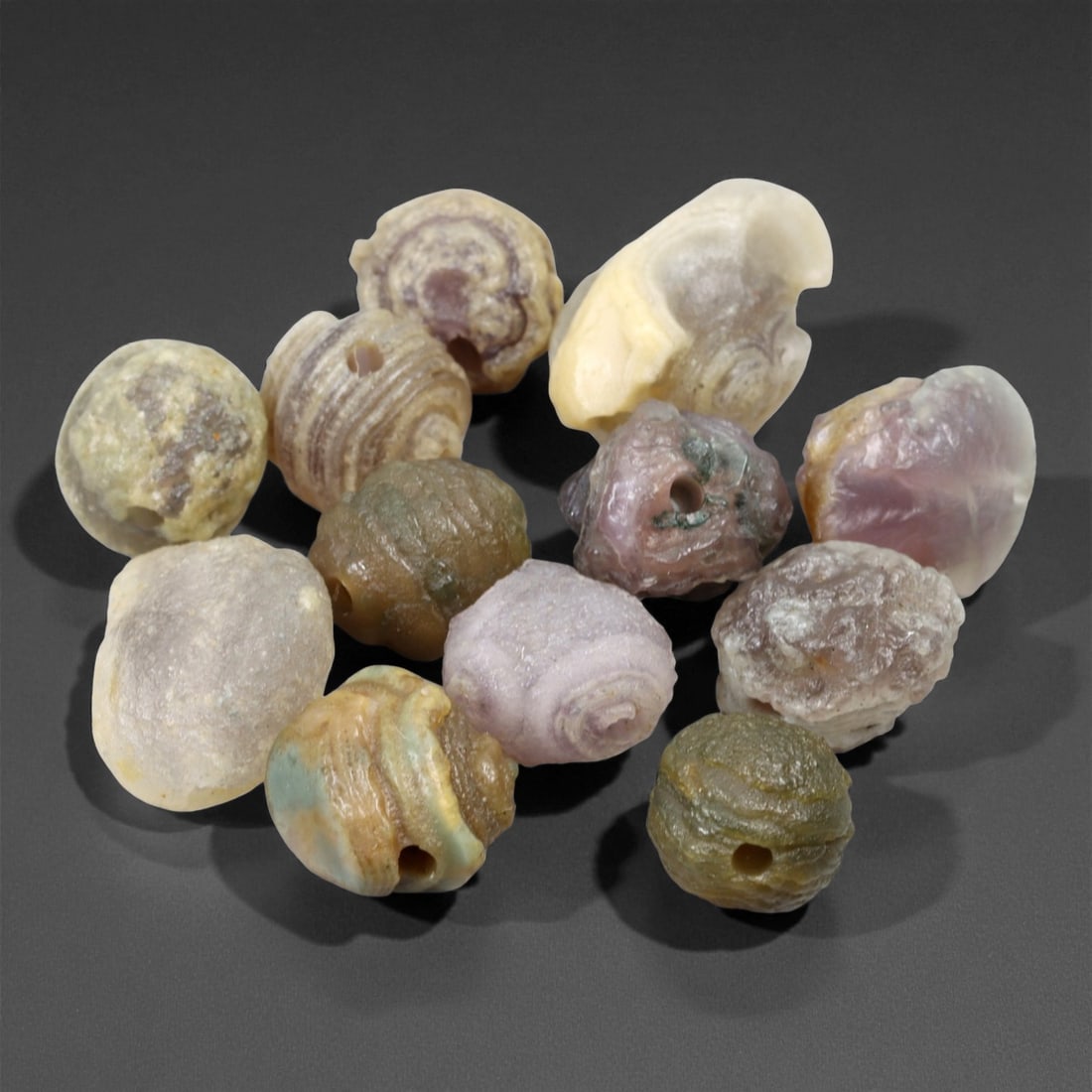 A Group of Mongolian Agate Eye Beads, 20th Century, 94FS: The group consists of twelve beads, carved from agate with natural concentric banding and eye-like formations. The beads display a range of colors, including green, pink, yellow, and translucent tones