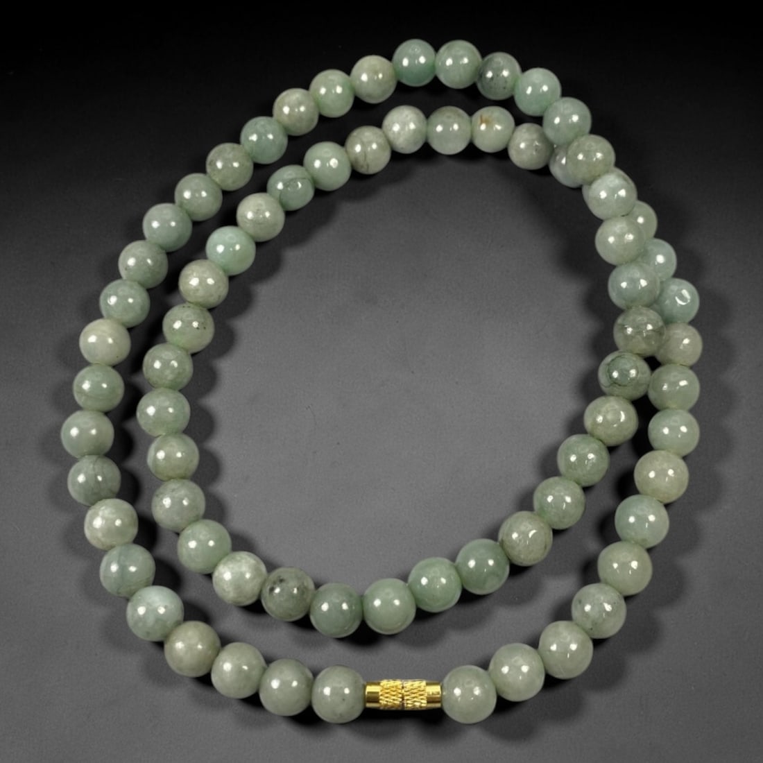 A Chinese Jadeite Jade Bead Necklace, 20th Century, 63ZK: Composed of spherical beads of uniform pale celadon green jadeite jade with subtle natural veining and minor internal inclusions, the necklace is strung in a continuous loop. The beads feature a smoot