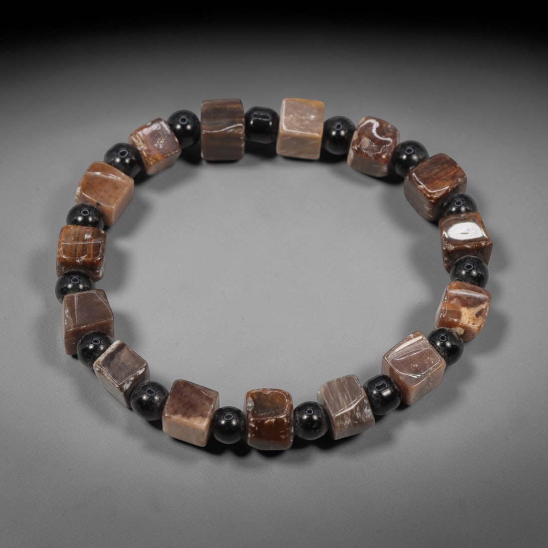A Chinese Fossilised Wood Bead Bracelet, 20th Century, 77FS: Composed of cushion-shaped beads of fossilised wood with natural banding and minor internal inclusions, the bracelet is strung in a continuous loop. The beads exhibit a smooth, polished surface with s