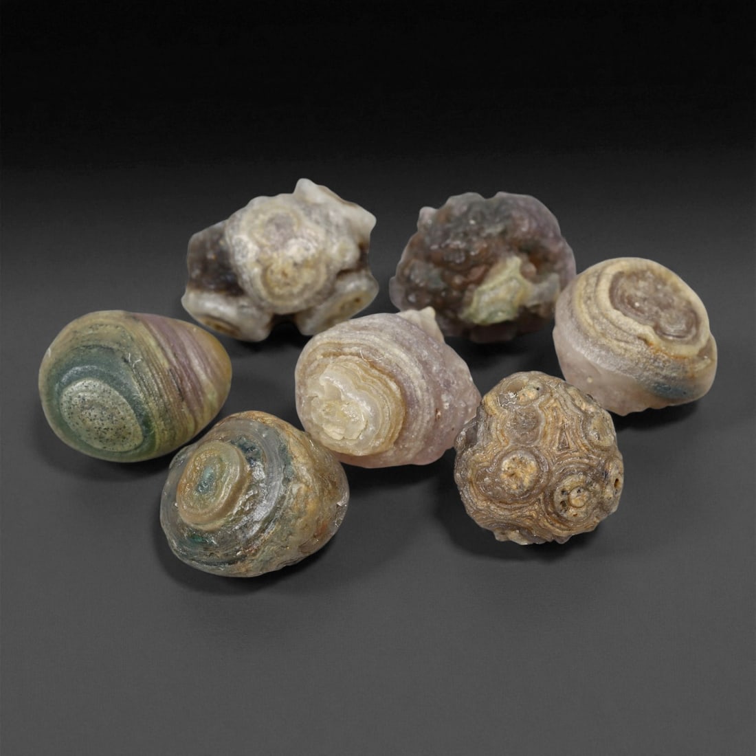 A Group of Mongolian Agate Eye Beads, 20th Century, 96FS: The group comprises six beads, formed from agate displaying prominent natural concentric banding and distinct eye-like formations. The specimens exhibit a palette of green, lavender, tan, and transluc