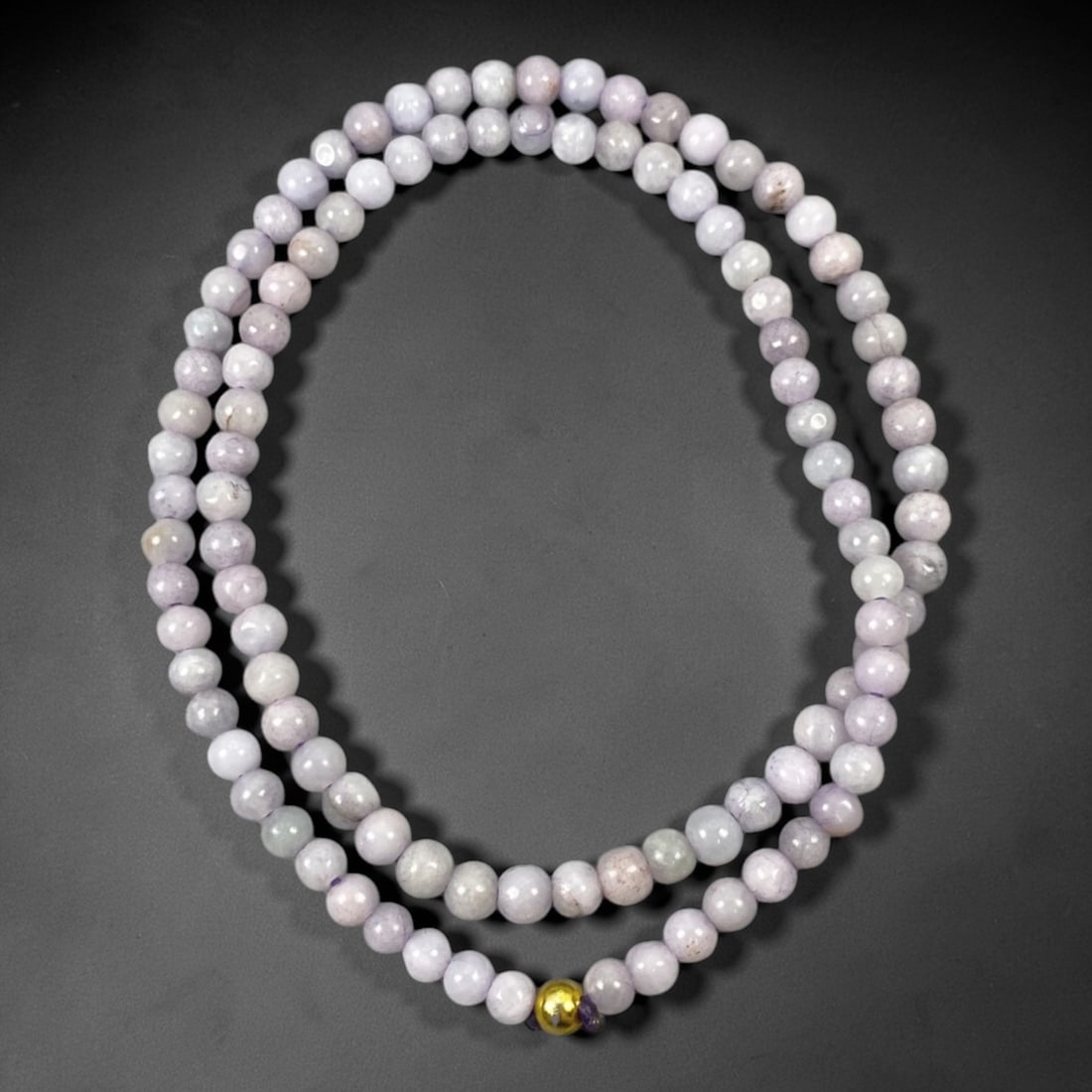 A Chinese Jadeite Jade Bead Necklace, 20th Century, 69ZK: Composed of spherical beads of pale lavender and white jadeite jade with natural veining and subtle tonal variations, the necklace is strung in a continuous loop. The beads exhibit a smooth, polished