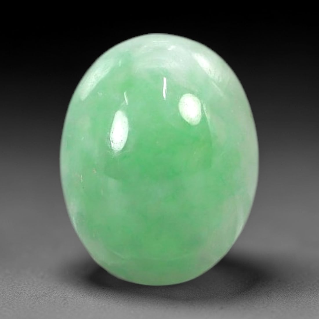 2.64 Carats Apple Green Burmese Jadeite Jade Cabochon - Natural Loose Gemstone, 15AC: This oval Burmese jadeite jade cabochon exhibits a soft apple green hue, with concentrated patches of richer green that add depth to its milky translucency. The smooth, domed cabochon cut enhances the