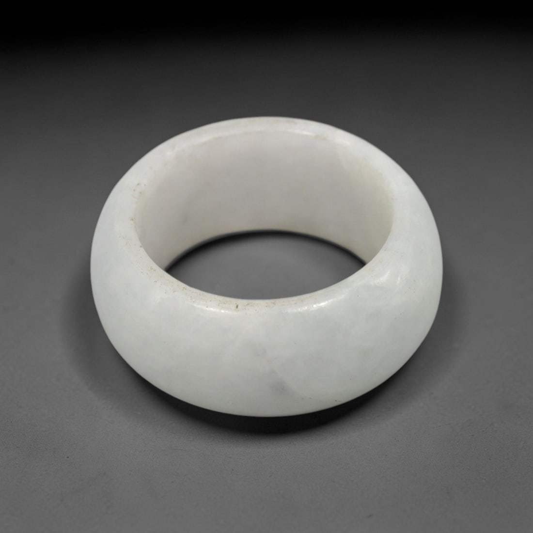 A Chinese Jadeite Jade Ring, 20th Century, 28FT: Carved from pale white jadeite jade with a smooth, highly polished surface, the ring is formed as a thick, circular band with a wide, slightly convex outer profile and a concave inner surface. The mat