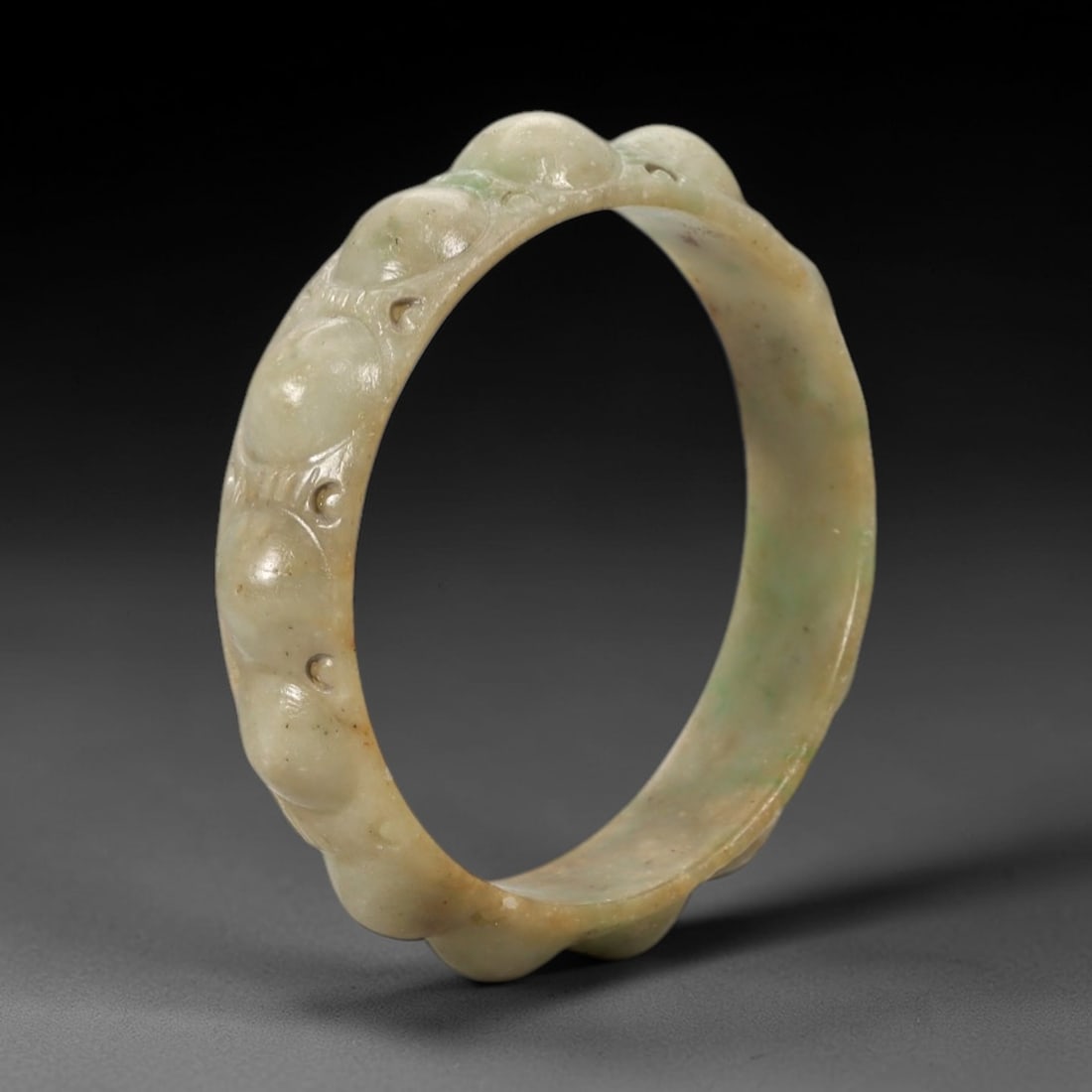 A Chinese Carved Jadeite Jade Bangle Bracelet, 20th Century, 62ZL: A petite jadeite bangle of circular form, elaborately carved in high relief with auspicious lingzhi fungus motifs that contour the entire circumference. The stone features a delicate pale celadon-gree