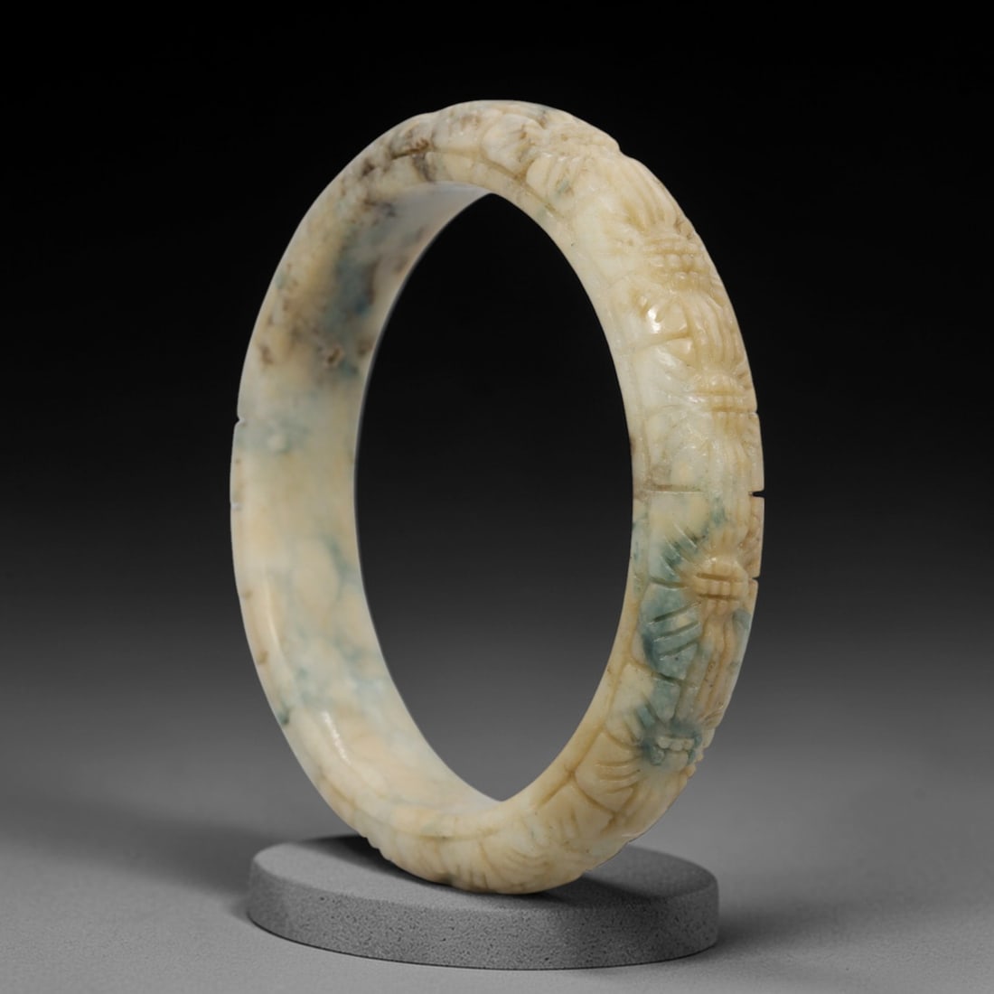 A Chinese Carved Jadeite Jade Bangle Bracelet, 20th Century, 51ZL: A fine jadeite bangle of flattened circular form, intricately carved in relief with a continuous band of foliate and floral motifs. The stone displays a captivating variegated palette, featuring a cre