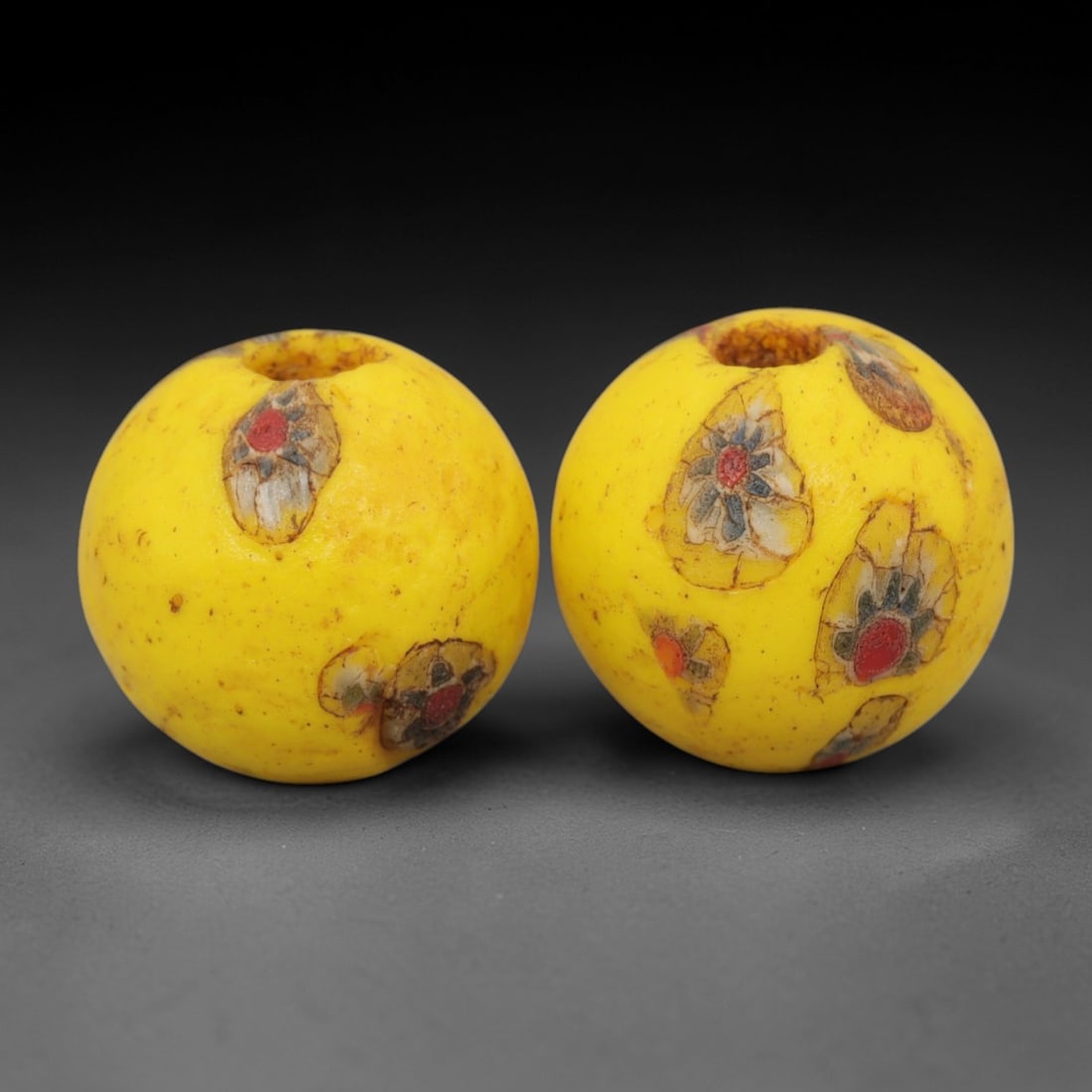 A Pair of Venetian Millefiori Glass Beads, 19th-20th Century, 48AD: Fabricated from opaque yellow glass, each bead is formed as a sphere with a central drilled perforation. The surface is decorated with characteristic millefiori canes, featuring floral and eye-like mo