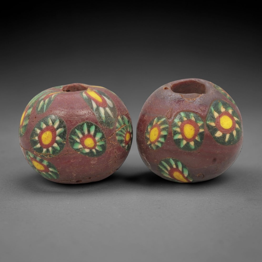A Pair of Venetian Millefiori Glass Beads, 19th-20th Century, 49AD: Fabricated from opaque reddish-brown glass, each bead is formed as a sphere with a central drilled perforation. The surface is decorated with characteristic millefiori canes, featuring circular floral