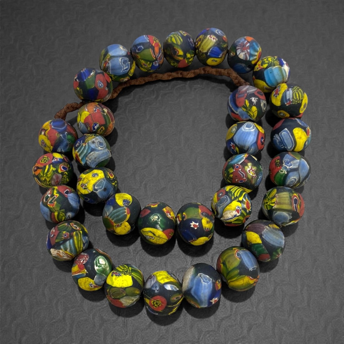 A Venetian Glass Millefiori Bead Necklace Strand, 19th Century, 11FR, 11FR: Composed of irregularly spherical glass beads decorated with millefiori canes, featuring a multi-colored mosaic pattern of deep blue, vibrant green, yellow, and red, strung on a modern braided fiber c