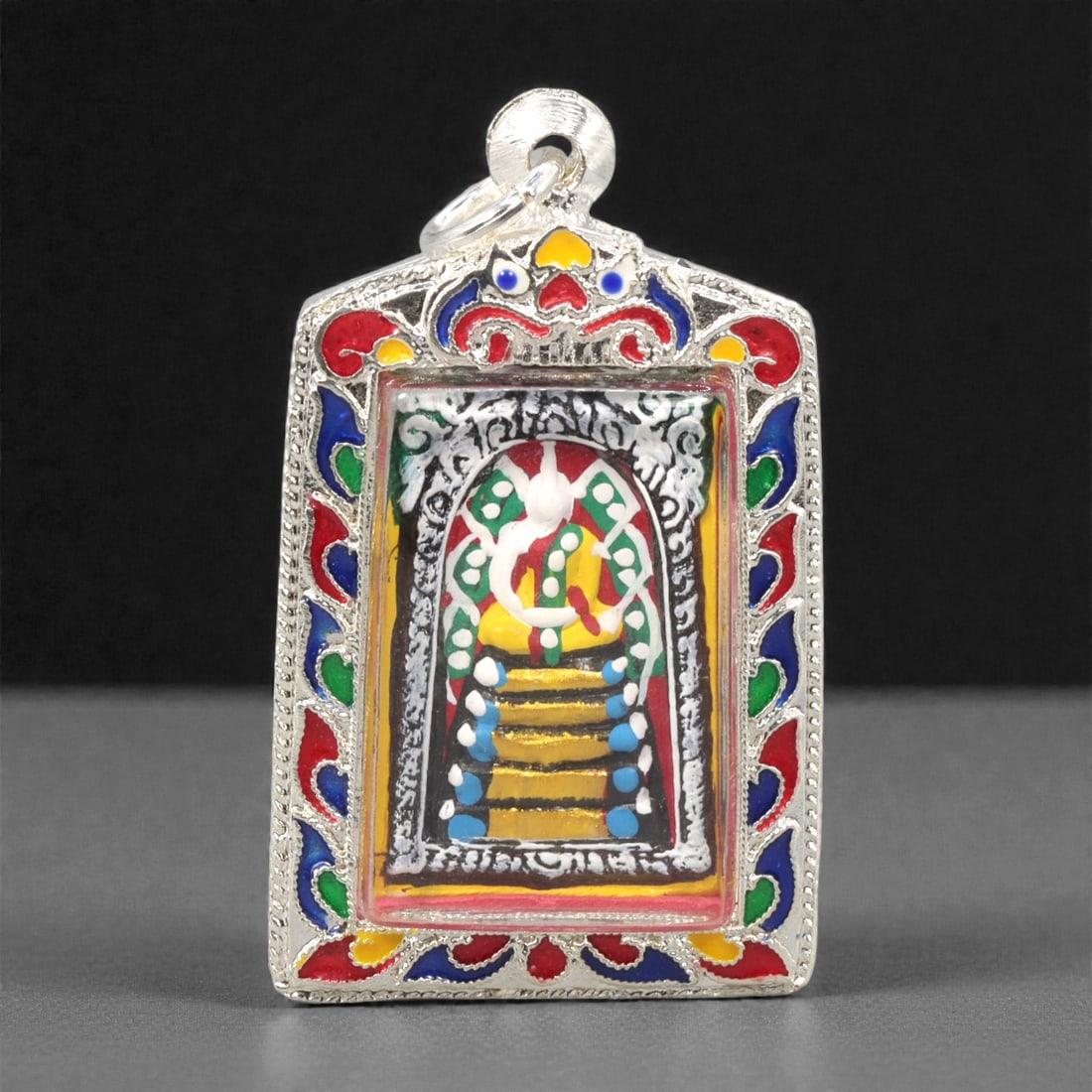 A Thai Painted Clay Buddhist Amulet, 20th Century, 23ZG: Molded from clay and finished with applied polychrome pigment, the amulet depicts a seated Buddha in meditation posture upon a tiered base, framed by an arched niche. The figure is rendered in low rel