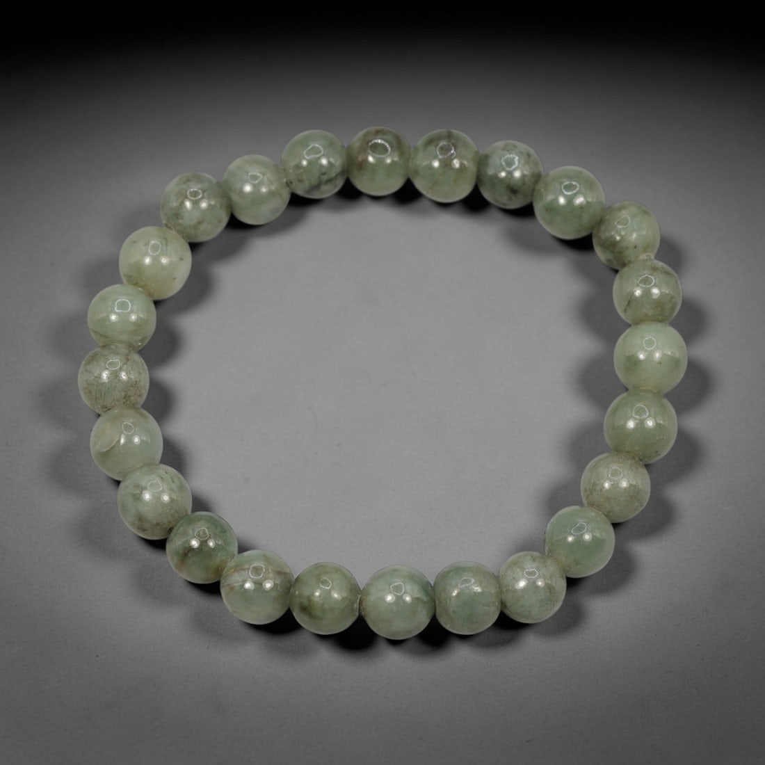A Chinese Jadeite Jade Bead Bracelet, 20th Century, 49ZK: Composed of a single strand of spherical jadeite jade beads forming a circular bracelet. The beads display natural tonal variation from pale green to light green, with visible internal mineral inclusi