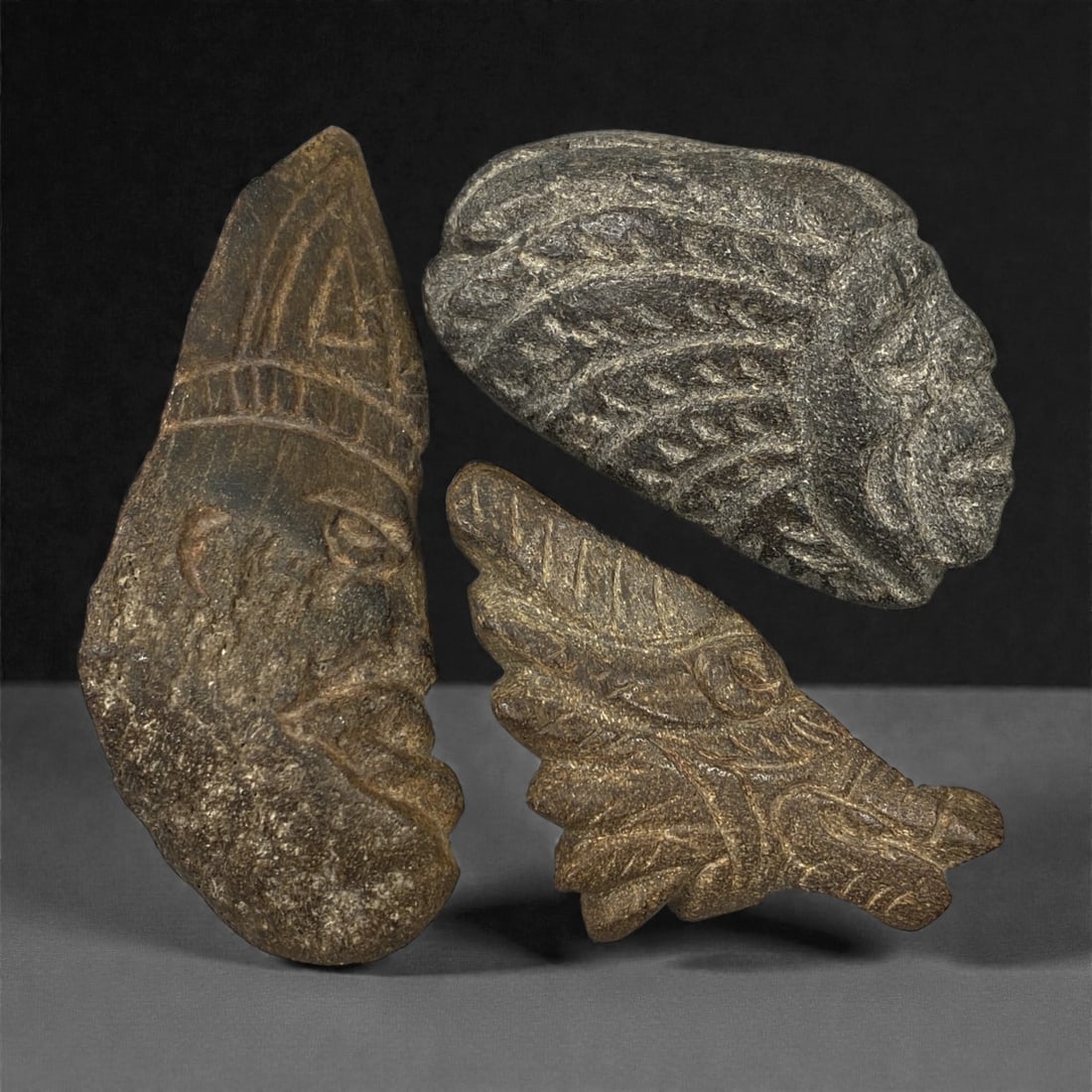 A Group of Three Pre-Columbian Stone Carvings, 10th-15th Century, 25FN: Carved from stone with natural tonal variation, mineral inclusions, and surface wear, the three carvings depict figural and zoomorphic forms in low to medium relief. The leftmost carving is vertically