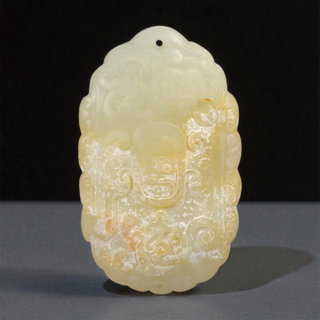 A Chinese Nephrite Jade Auspicious Plaque, 20th Century, 42FB: Carved from pale cream-colored nephrite jade with areas of translucency and scattered russet inclusions, the plaque is worked in relief on one face with dense auspicious ornament. The upper section is