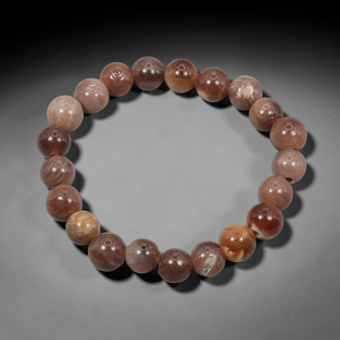 A Chinese Fossilised Wood Bead Bracelet, 20th Century, 54ZK: Composed of a single strand of spherical fossilised wood beads forming a circular bracelet. The beads display natural tonal variation from pale beige to deep brown, with visible linear wood-grain patt