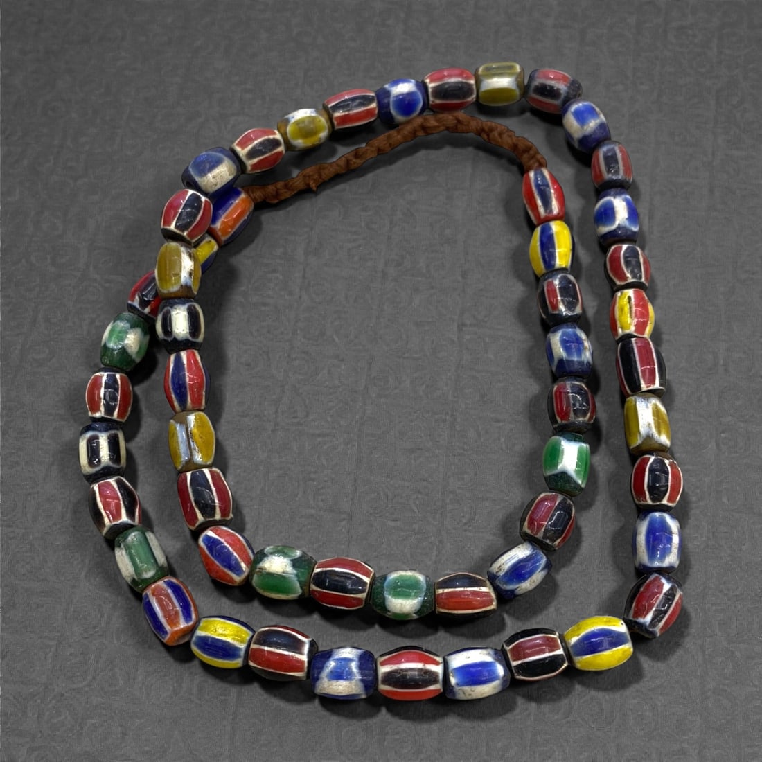 A Venetian Glass Chevron Bead Necklace Strand, 19th Century, 10FR, 10FR: Composed of cylindrical glass beads decorated with concentric chevron patterns in red, blue, white, yellow, and green, strung on a modern braided fiber cord. The layered chevron design is a hallmark o