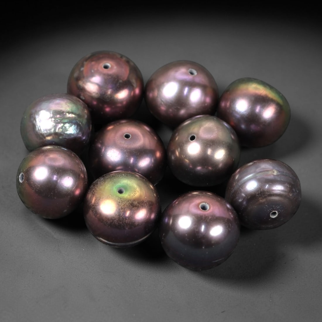 A Group of Ten Baroque Cultured Pearls, 99ZH: Comprising ten baroque cultured pearls, each of spherical to slightly irregular form with a deep metallic purple hue and subtle iridescent overtones. Each pearl features a small, precisely drilled hol