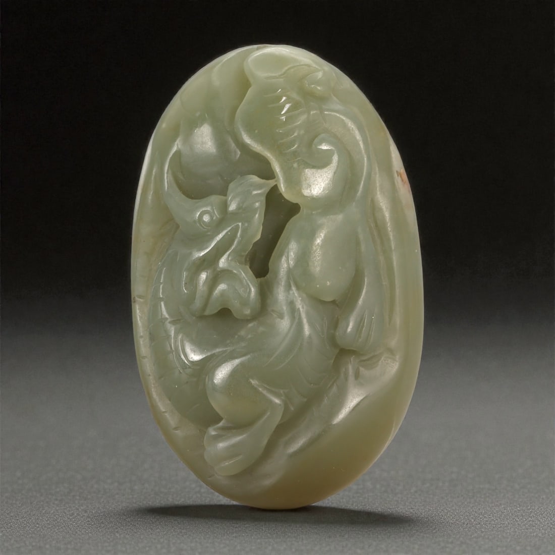 A Chinese Jade Fruit and Flower Plaque, 20th Century, 43YA: Carved from pale celadon jade with soft translucency and minor natural inclusions, the object is formed as an oval plaque carved in relief. The composition depicts a fruiting plant with a rounded frui