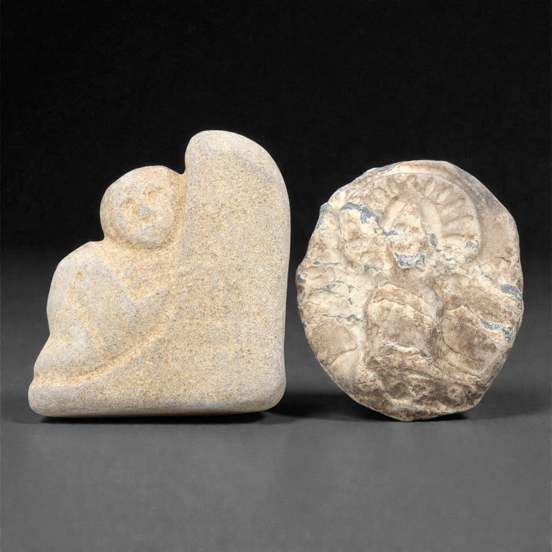 Two Japanese Stone Monk Figures, Edo Period, 99ZG: The first figure is carved from light beige stone with a fine, granular texture. It depicts a seated monk integrated with a larger, irregular stone block, with a rounded head, simplified facial featur