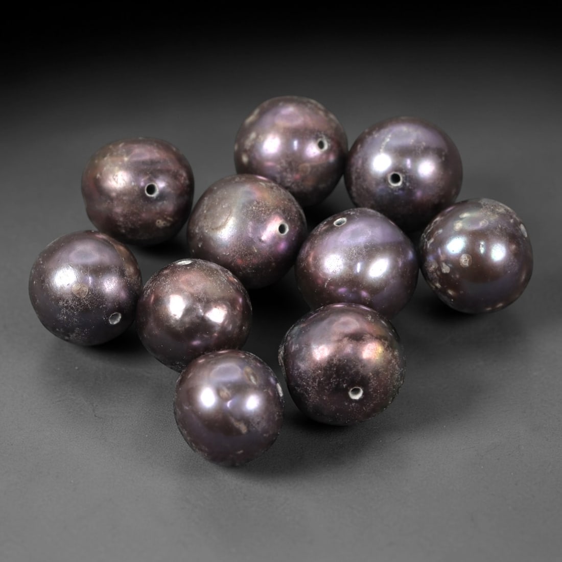 A Group of Ten Baroque Cultured Pearls, 26XM: Comprising ten baroque cultured pearls, each of spherical to slightly irregular form with a deep metallic purple hue and subtle iridescent overtones. Each pearl features a small, precisely drilled hol