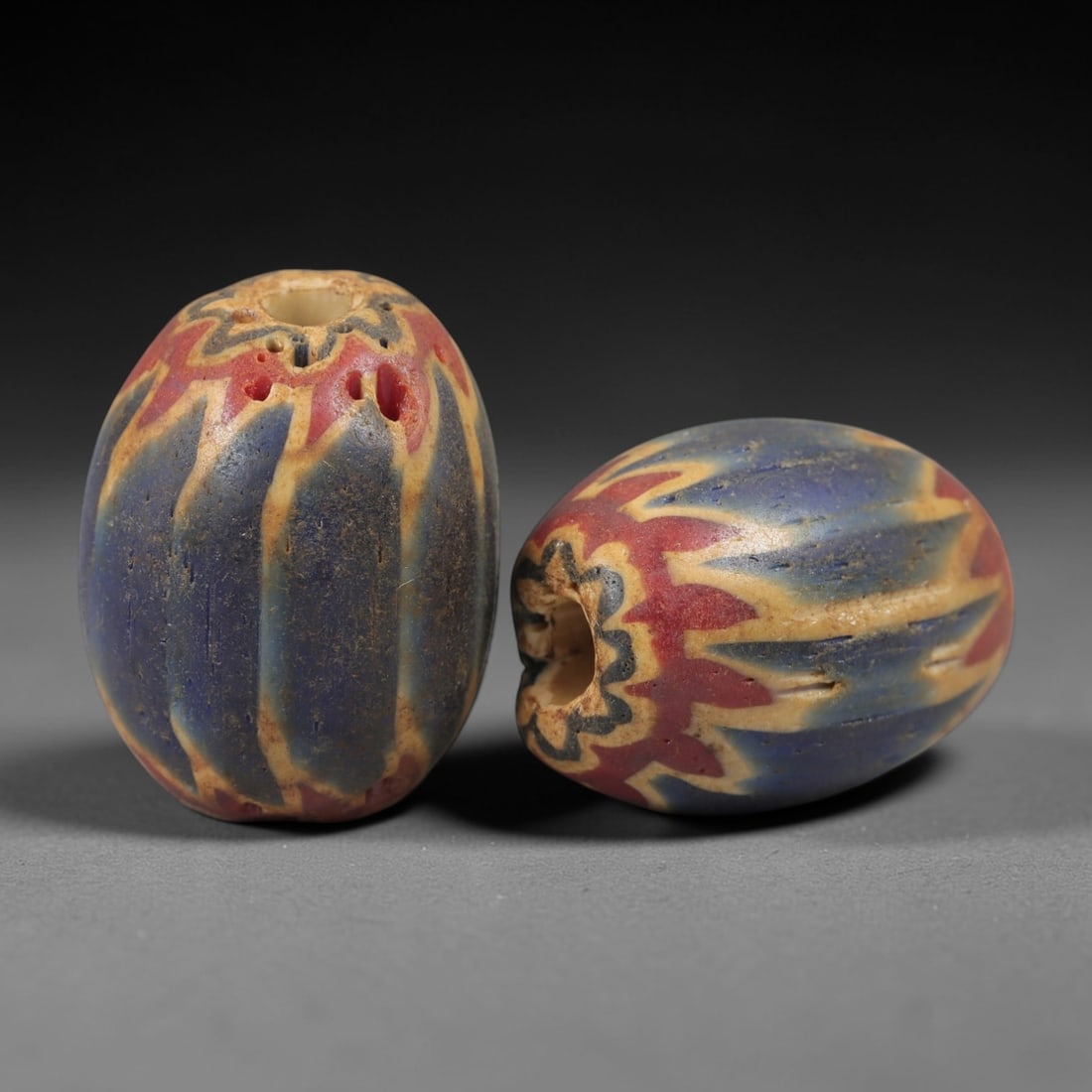 A Pair of Venetian Glass Chevron Beads, 18th-19th Century, 87AC: Crafted from translucent glass with a pale yellow core, each bead is decorated with a chevron pattern of alternating deep blue and vibrant red layers, radiating from the central perforation to the out