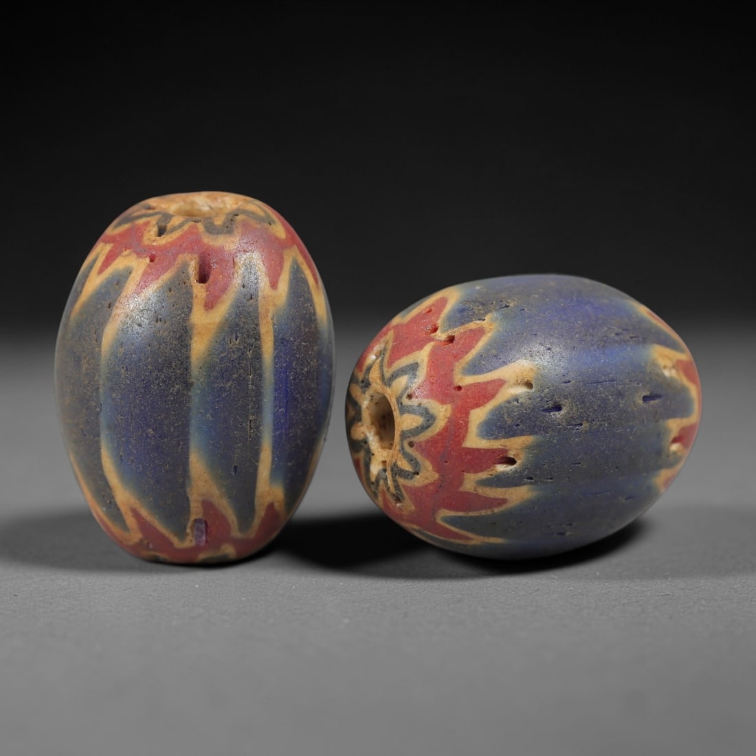 A Pair of Venetian Glass Chevron Beads, 18th-19th Century, 86AC: Crafted from translucent glass with a pale yellow core, each bead is decorated with a chevron pattern of alternating deep blue and vibrant red layers, radiating from the central perforation to the out